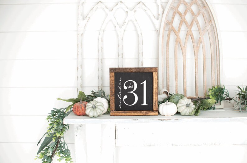 May include: A wooden framed chalkboard with the number 31 in white, with a spider and floral accents. The chalkboard is surrounded by pumpkins and greenery, creating a festive Halloween display.