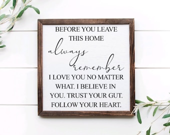 May include: A white wooden sign with a brown frame, featuring the text "BEFORE YOU LEAVE THIS HOME always remember I LOVE YOU NO MATTER WHAT. I BELIEVE IN YOU. TRUST YOUR GUT. FOLLOW YOUR HEART."