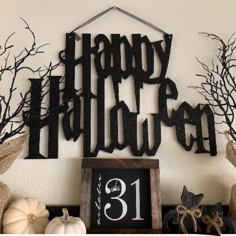 May include: A black glitter "Happy Halloween" sign hangs above a wooden framed chalkboard displaying the number "31" and a spider graphic. White and orange pumpkins and black cat decorations complete the scene.