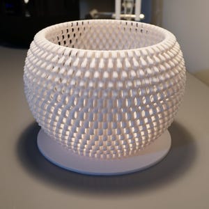 May include: A white, spherical decorative basket with a woven, openwork design. The basket sits on a round base, creating a unique texture and pattern. The open design allows light to filter through, creating a play of light and shadow.