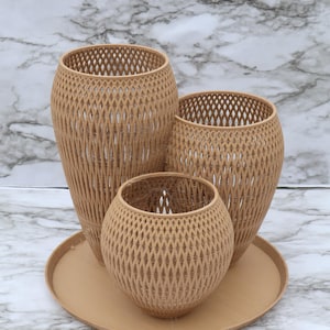 May include: Three decorative woven vases in varying sizes, arranged on a round tray. The vases have a diamond-patterned design and a light brown color. The background is a marble-patterned surface.