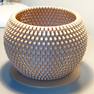 May include: A decorative, spherical wooden bowl with a woven pattern. The light-colored wood is arranged in a repeating, interlocking design. The bowl sits on a round, light-colored base. The interior is visible through the openings.