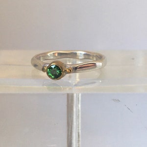 Puede incluir: Un anillo de plata con una piedra preciosa verde y detalles dorados.