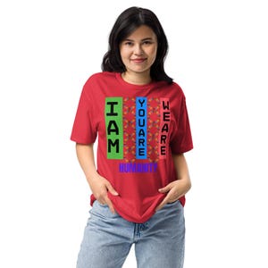 May include: A red t-shirt with the words "I AM YOU ARE WE ARE HUMANITY" printed vertically in green, blue, and pink. The shirt is made of a soft material and is being worn.