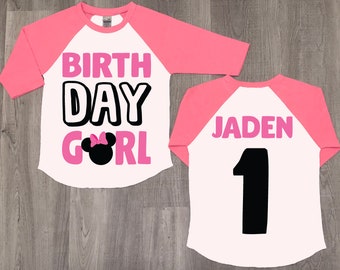May include: A white and pink baseball-style shirt with the words "BIRTH DAY GIRL" in pink and black, and a Minnie Mouse graphic. The back of the shirt has the name "JADEN" and the number "1" in black.