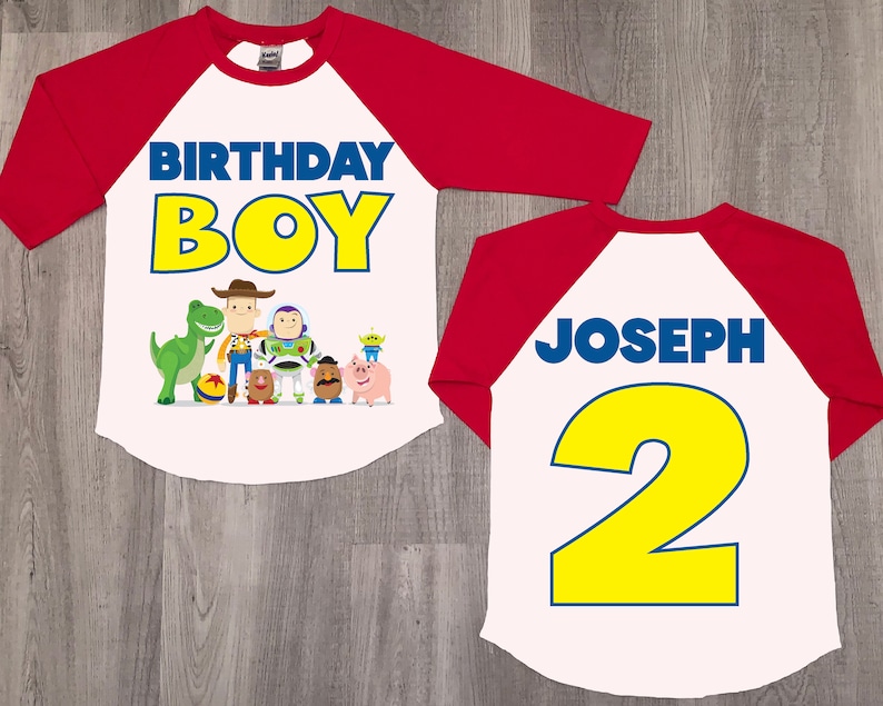 K&ouml;nnte beinhalten: Rotes und wei&szlig;es Baseball-Shirt mit Toy Story-Motiv. Die Vorderseite des Shirts tr&auml;gt den Schriftzug "Birthday Boy" mit einer Gruppe von Toy Story-Charakteren. Die R&uuml;ckseite des Shirts tr&auml;gt den Schriftzug "Joseph 2" in Blau und Gelb.
