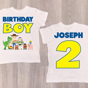 K&ouml;nnte beinhalten: Zwei wei&szlig;e T-Shirts mit einem Toy Story-Motiv. Die Vorderseite des Shirts zeigt in gelben Buchstaben mit blauen Umrandungen den Schriftzug "Birthday Boy" und eine Gruppe von Toy Story-Charakteren. Die R&uuml;ckseite des Shirts zeigt in gelben Buchstaben mit blauen Umrandungen den Schriftzug "Joseph 2".