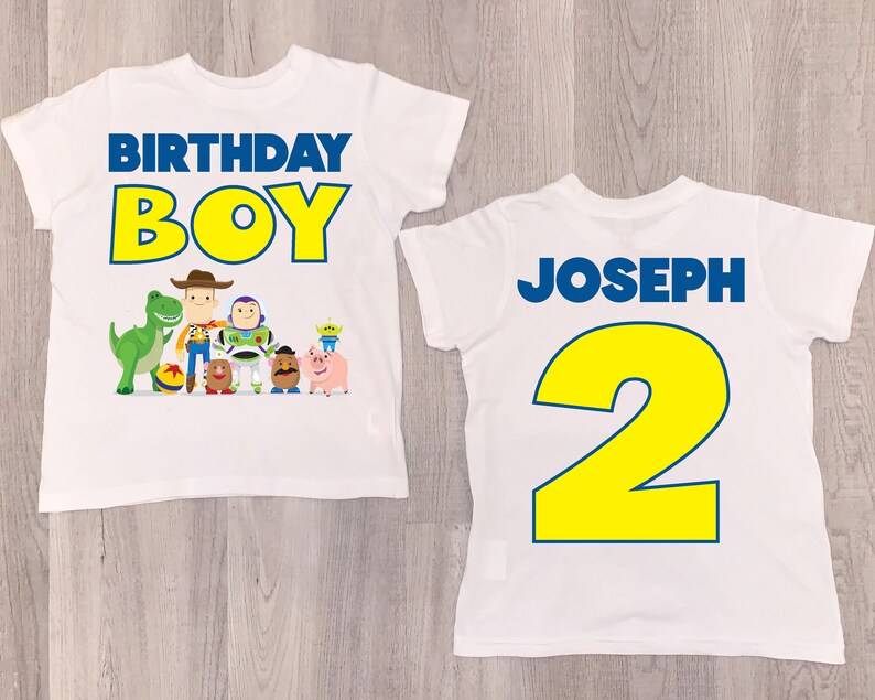 K&ouml;nnte beinhalten: Zwei wei&szlig;e T-Shirts mit einem Toy Story-Motiv. Die Vorderseite des Shirts zeigt in gelben Buchstaben mit blauen Umrandungen den Schriftzug "Birthday Boy" und eine Gruppe von Toy Story-Charakteren. Die R&uuml;ckseite des Shirts zeigt in gelben Buchstaben mit blauen Umrandungen den Schriftzug "Joseph 2".