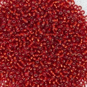Peut inclure: Gros plan sur un tas de petites perles rondes rouges. Les perles sont densément tassées, créant une surface texturée. Elles ont une finition brillante et semblent être en verre ou dans un matériau similaire. Elles sont probablement utilisées pour la fabrication de bijoux ou d'autres travaux manuels.