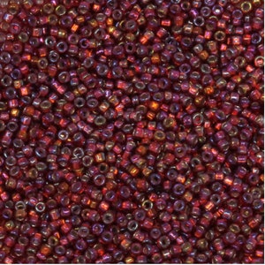 Op de afbeelding: Een close-up van een grote hoeveelheid kleine, ronde, rode iriserende glazen kralen. De kralen hebben een metallic glans en zijn perfect voor het maken van sieraden.