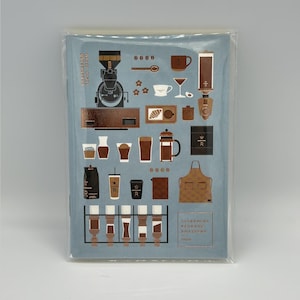 May include: A blue notebook with gold and brown illustrations of coffee-making equipment and accessories. The notebook features a coffee grinder, cups, a French press, and an apron. Text on the notebook reads "NAKAMEGURO TOKYO JAPAN" and "STARBUCKS RESERVE ROASTERY TOKYO".