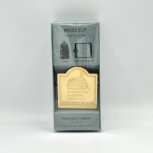 May include: A gold-colored brass clip from Traveler's Company, made in Japan. The clip features the Starbucks Reserve Roastery logo and is packaged in a gray box with the text "BRASS CLIP" and "MADE IN JAPAN".