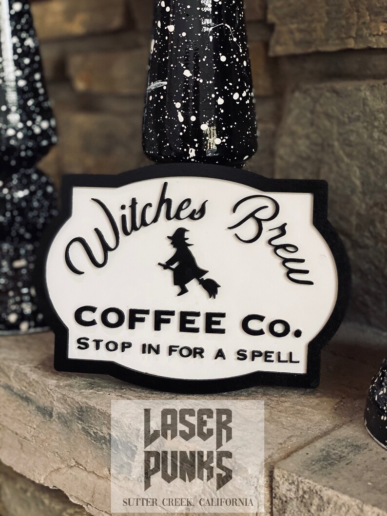 May include: Black and white sign with the text "Witches Brew Coffee Co. Stop in for a spell" and a silhouette of a witch riding a broomstick. The sign is on a stone surface with a black and white splatter paint background.