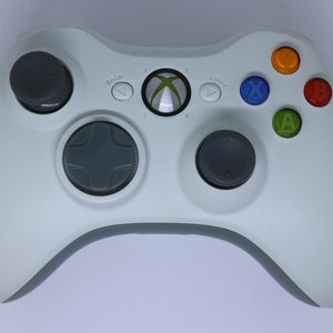 May include: A white Xbox 360 controller with gray buttons and a green Xbox logo. The controller has a directional pad, four face buttons labeled A, B, X, and Y, and two analog sticks.