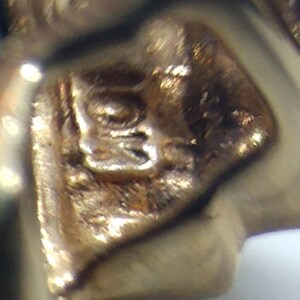 May include: Close-up of a gold-colored metal stamp with an intricate design. The stamp is likely used for jewelry or other metal crafts.