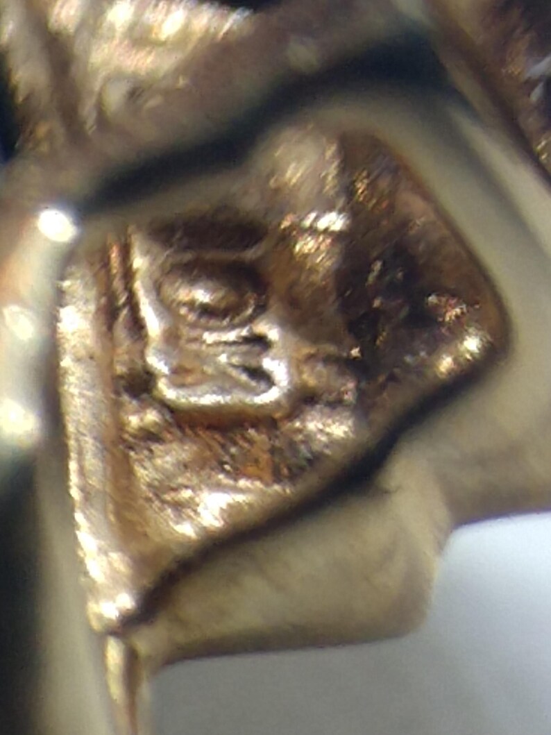 May include: Close-up of a gold-colored metal stamp with an intricate design. The stamp is likely used for jewelry or other metal crafts.