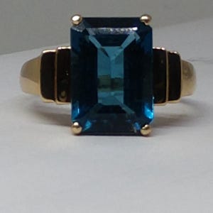 May include: A gold ring with a large, deep blue, emerald-cut gemstone.