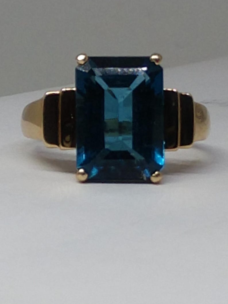 May include: A gold ring with a large, deep blue, emerald-cut gemstone.