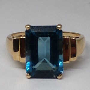 May include: A gold ring with a large, rectangular, blue topaz gemstone.