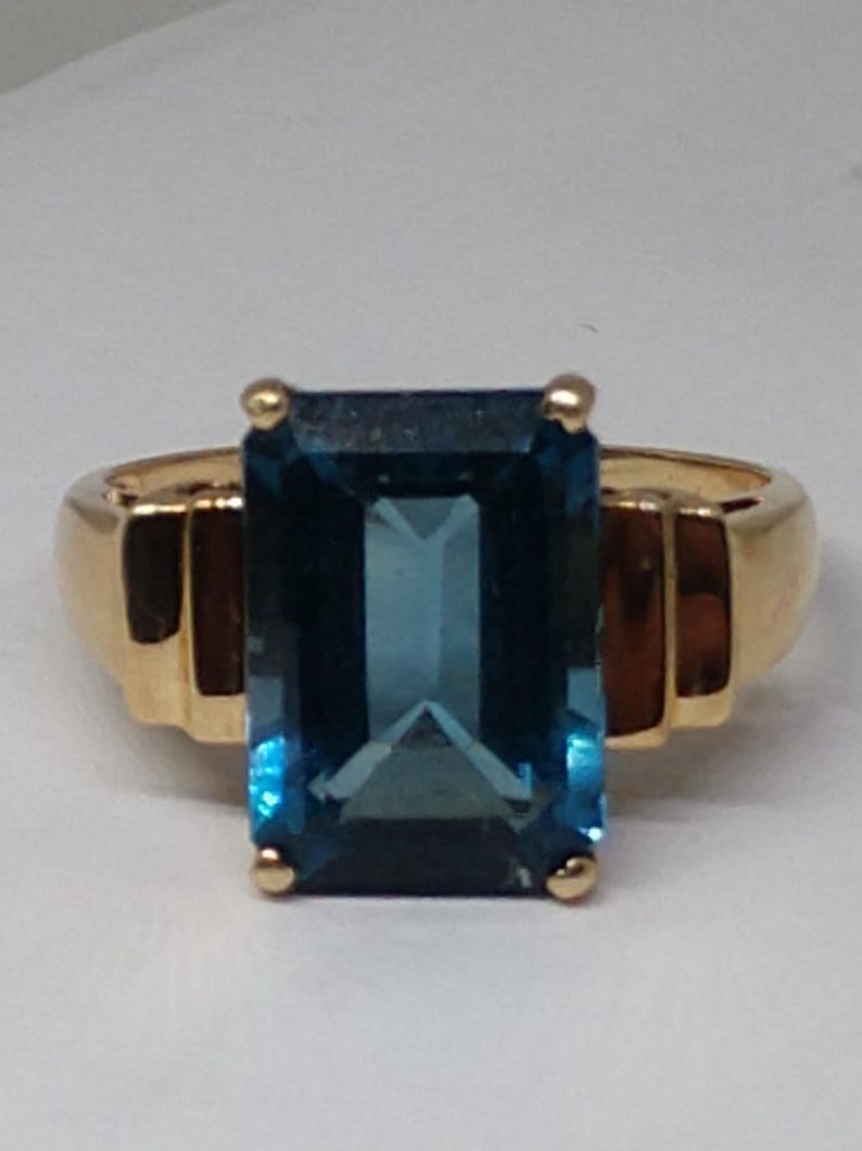 May include: A gold ring with a large, rectangular, blue topaz gemstone.