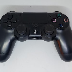 May include: A black PlayStation 4 DualShock 4 wireless controller with a textured surface. The controller has a directional pad, four face buttons, two analog sticks, and two shoulder buttons.