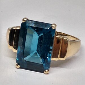 May include: A gold ring with a large, rectangular, blue topaz gemstone.