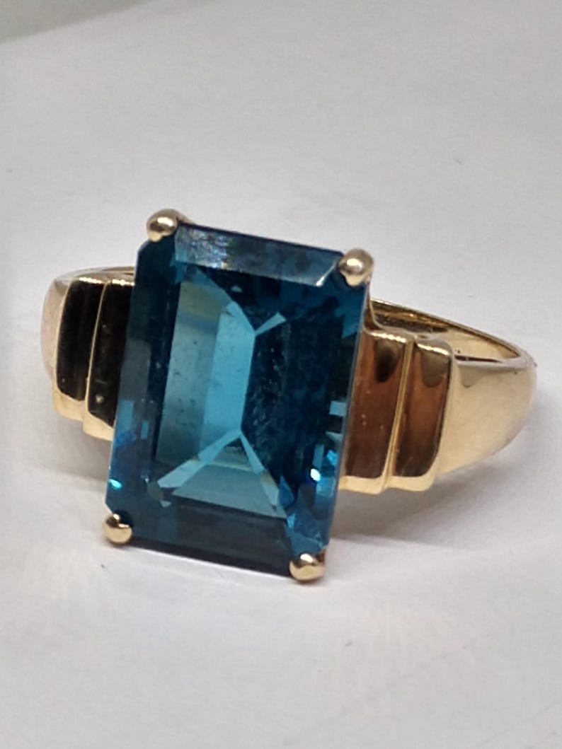 May include: A gold ring with a large, rectangular, blue topaz gemstone.