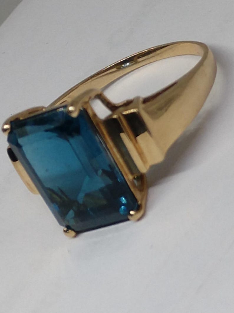 May include: A gold ring with a large, rectangular, blue gemstone.