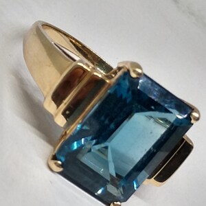 May include: A gold ring with a large, rectangular, blue topaz gemstone.