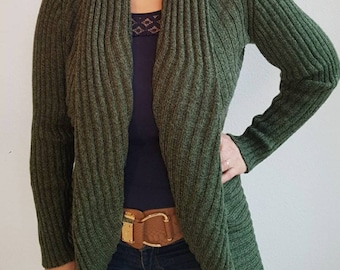 May include: A dark green knitted cardigan with a draped, asymmetrical front. The cardigan has a ribbed texture and a wide, open collar.