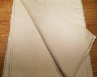 May include: A folded, cream-colored blanket with a soft, textured appearance. The blanket is neatly folded, revealing the edges and seams. The neutral colour and simple design suggest a cosy, versatile home textile.