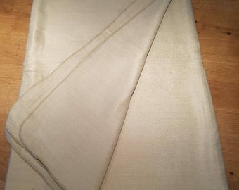 May include: A folded, cream-coloured blanket with a slight sheen. The blanket is made of a soft, woven material and has a folded edge. The blanket is on a wooden surface.