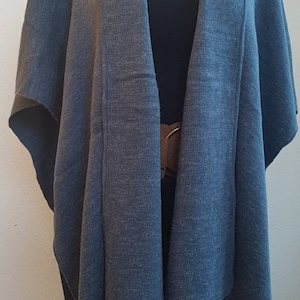 Könnte beinhalten: Ein blauer Strickponcho mit langem, fließendem Design. Der Poncho hat einen V-Ausschnitt und einen schlichten, eleganten Stil.