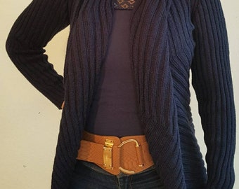 May include: A navy blue knitted cardigan with a draped front and long sleeves. The cardigan is worn over a dark blue tank top and brown belt with a gold buckle.