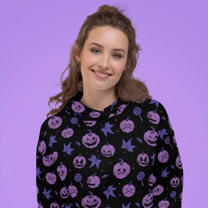 Könnte beinhalten: Schwarzer Hoodie mit einem lila-schwarzen Halloween-Kürbis-Muster. Der Hoodie hat eine Kapuze mit Kordelzug und eine Kängurutasche.