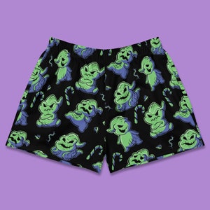 Könnte beinhalten: Schwarze Shorts mit einem sich wiederholenden Muster aus grünen und blauen Comicfiguren mit einem verschmitzten Grinsen. Die Figuren sind von Zuckerstangen und kleinen schwarzen Würmern umgeben.