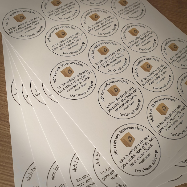 Puede incluir: Varias pegatinas redondas marrones y blancas con el texto "Ich bin wiederverwendet", que se traduce como "Soy reutilizado" en ingl&eacute;s. Las pegatinas presentan una peque&ntilde;a caja marr&oacute;n con un coraz&oacute;n y el texto "Der Umwelt zuliebe", que se traduce como "Por el bien del medio ambiente" en ingl&eacute;s.