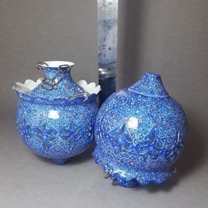 May include: Two blue and white ceramic hanging lanterns with intricate cut-out designs. The lanterns have a white interior and are decorated with a floral pattern.