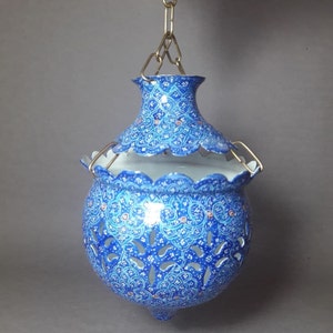 May include: A blue and white hanging lamp with intricate floral patterns and cutouts. The lamp is made of metal and has a chain for hanging.