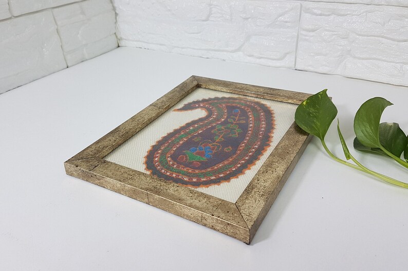 May include: A framed artwork featuring a colorful paisley design in shades of orange, green, blue, and purple. The frame is a distressed gold color.