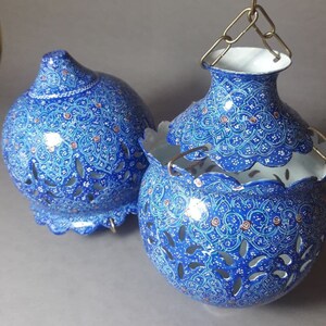 May include: Two blue and white decorative hanging lanterns with intricate floral patterns and cut-out designs. The lanterns are made of metal and have a white interior.