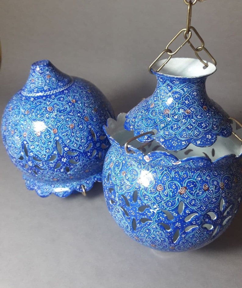 May include: Two blue and white decorative hanging lanterns with intricate floral patterns and cut-out designs. The lanterns are made of metal and have a white interior.