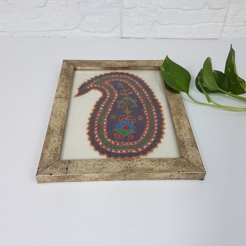 May include: A framed paisley design with intricate embroidery in shades of orange, green, blue, and purple on a white background.