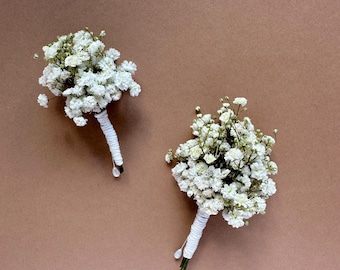 Può includere: Due piccoli bouquet di fiori bianchi di gipsofila, ciascuno con uno stelo avvolto di bianco. I bouquet sono posti su uno sfondo marrone uniforme. I fiori sono in piena fioritura.