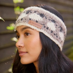 May include: A woman wearing a grey and white knitted headband with a brown leather label that says "Pachamama".