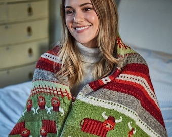 Può includere: Una donna seduta su un letto avvolta in una coperta di lana verde, rossa e grigia con un motivo di mucche delle Highlands.