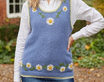 May include: A blue knitted vest with a white daisy and green leaf embroidery design. The vest has a scoop neck and a ribbed trim.