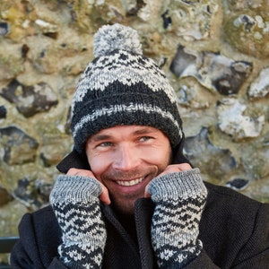 Peut inclure: Une personne porte un bonnet en tricot gris et noir avec un pompon et des mitaines assorties. Le bonnet et les mitaines ont un motif géométrique. La personne porte un manteau gris foncé.
