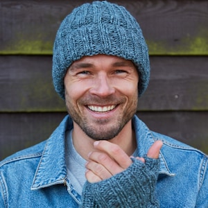 Könnte beinhalten: Ein Mann trägt eine blaue Jeansjacke und eine blaue Strickmütze und Fingerhandschuhe. Er lächelt.