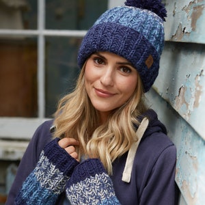 May include: A blue and white striped knitted hat with a pom pom on top. The hat is worn by a person with blonde hair. The person is also wearing blue and white striped knitted fingerless gloves.